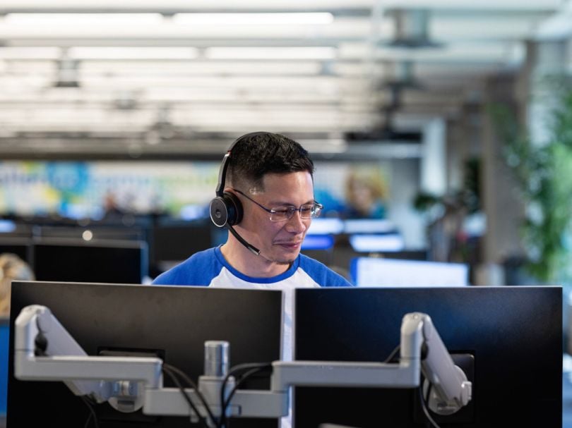 An Alliant Credit Union employee works at his computer in the office while wearing a headset